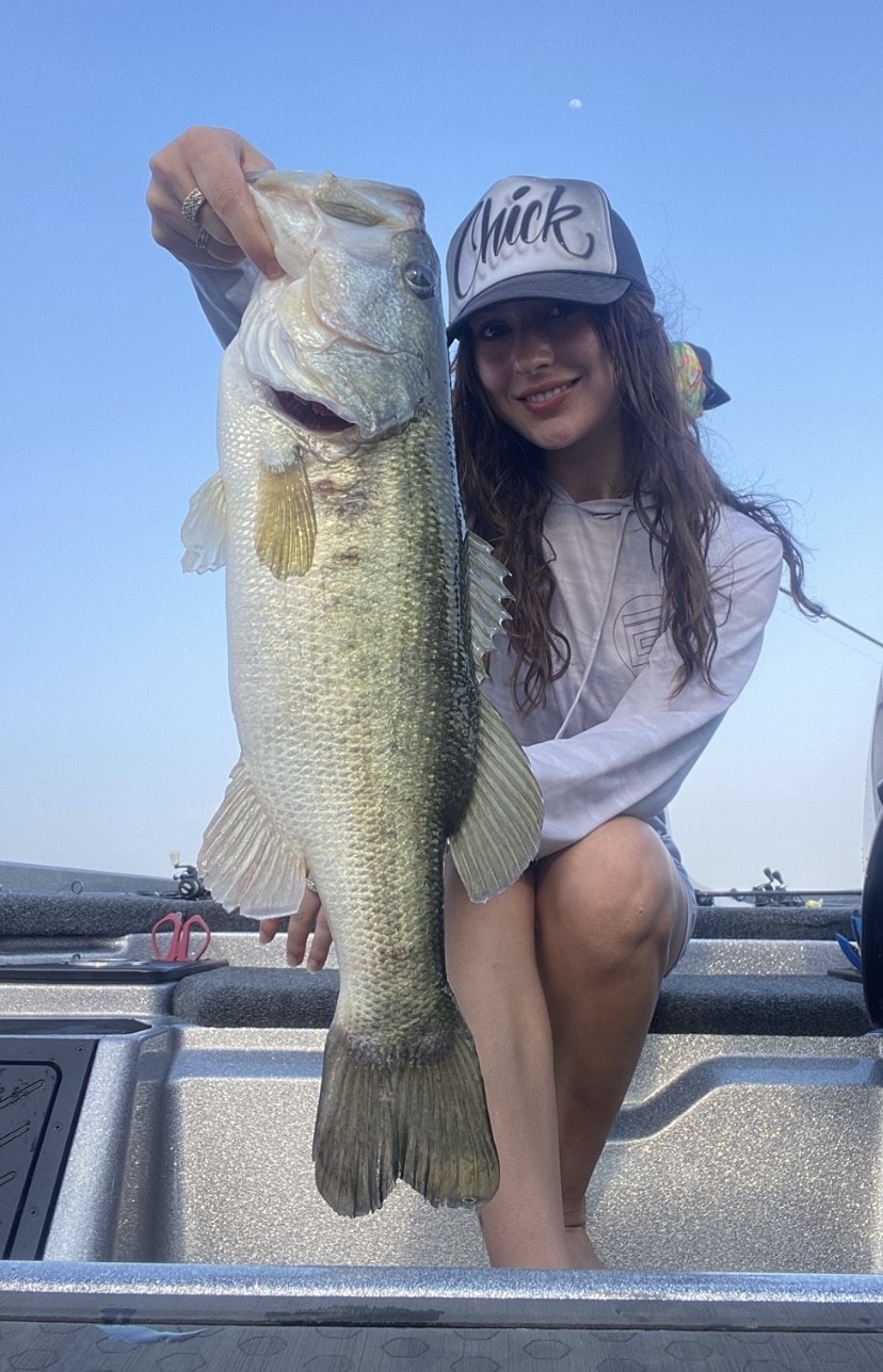 Girl in Chick cap holding massive bass on bright day