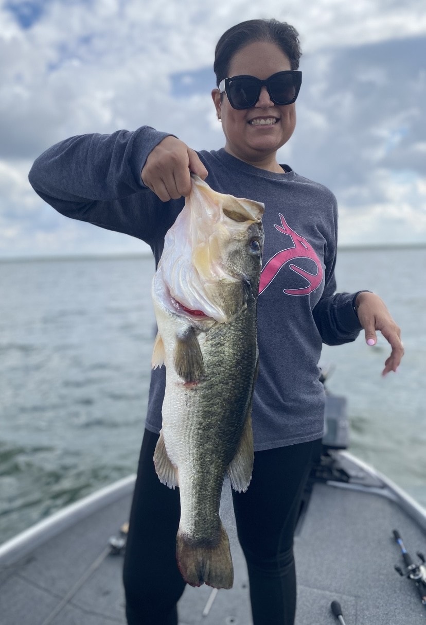 Woman in Realtree shirt holding big bass on cloudy day