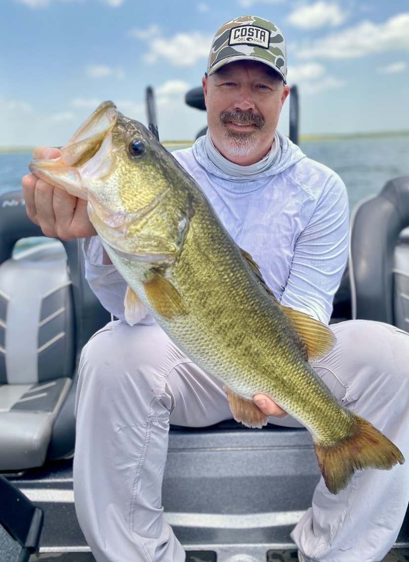 Man in Costa cap holding trophy bass on boat