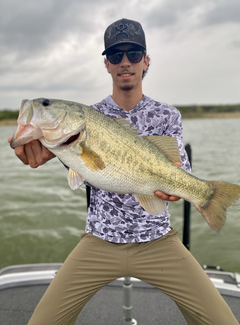 Young man in camo shirt holding big bass on cloudy day
