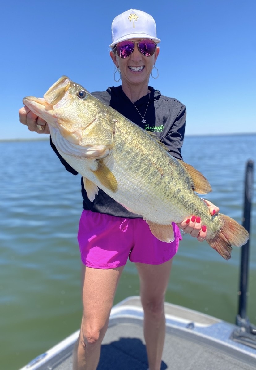 Woman in white palm tree cap holding giant bass on sunny day