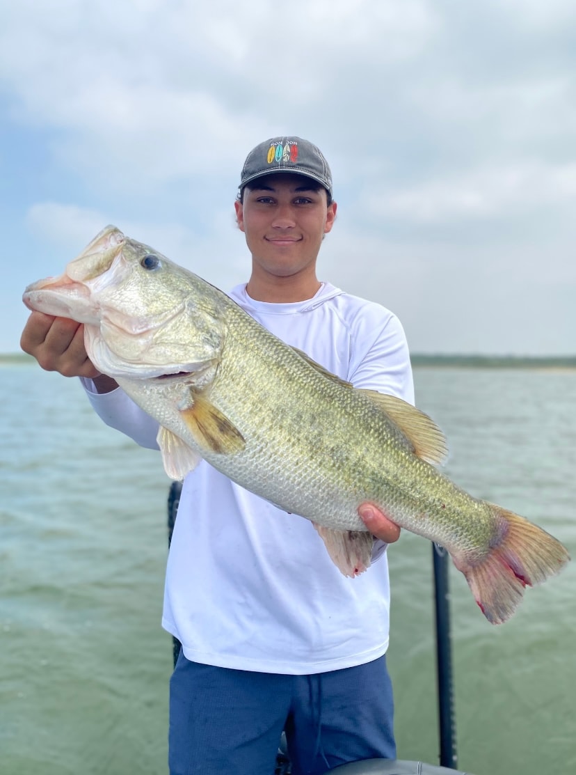 Young man in Ron Jon cap holding big bass on cloudy day