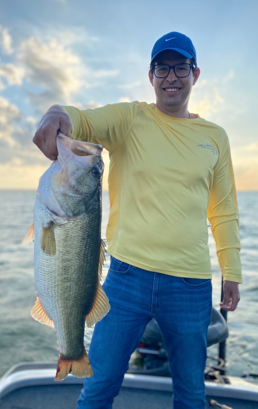 Man in yellow shirt and Nike cap holding bass at sunset