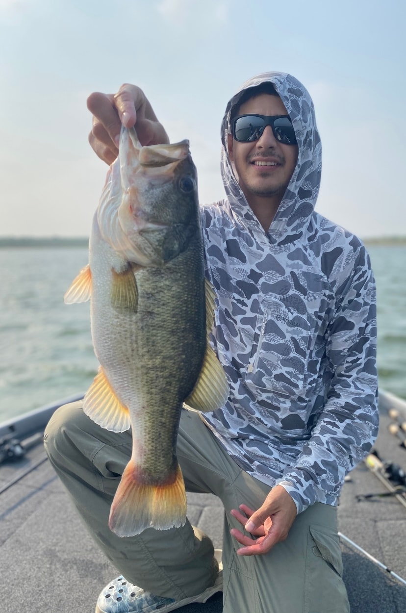 Man in camo hoodie holding bass by the lip on sunny day