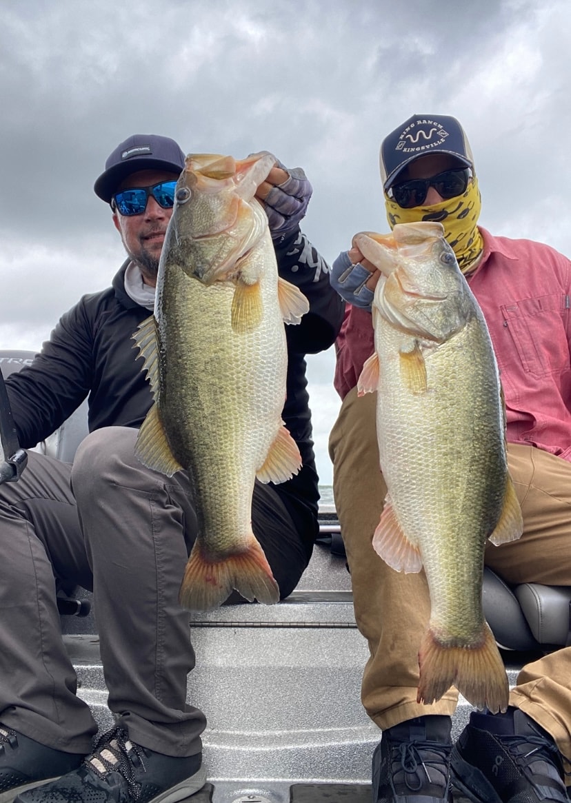 Two anglers holding massive bass on stormy day