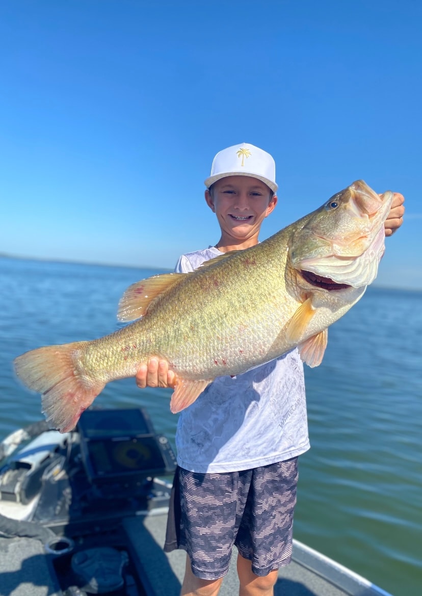 Young boy in white palm tree cap holding massive bass