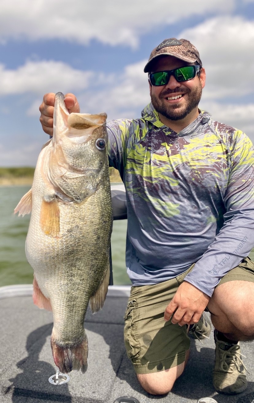 Man in Cabelas cap holding big bass on cloudy day