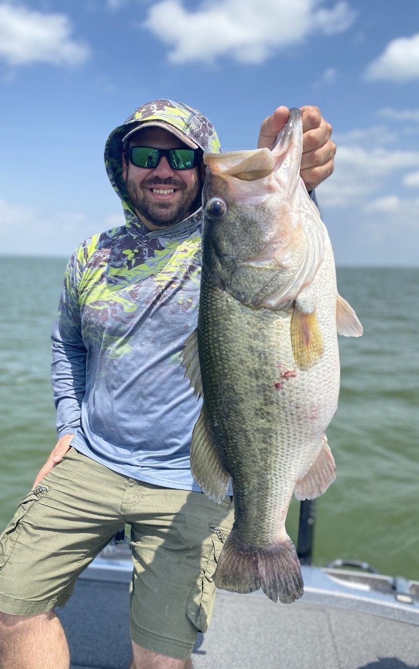 Man in camo hoodie holding giant bass on open water