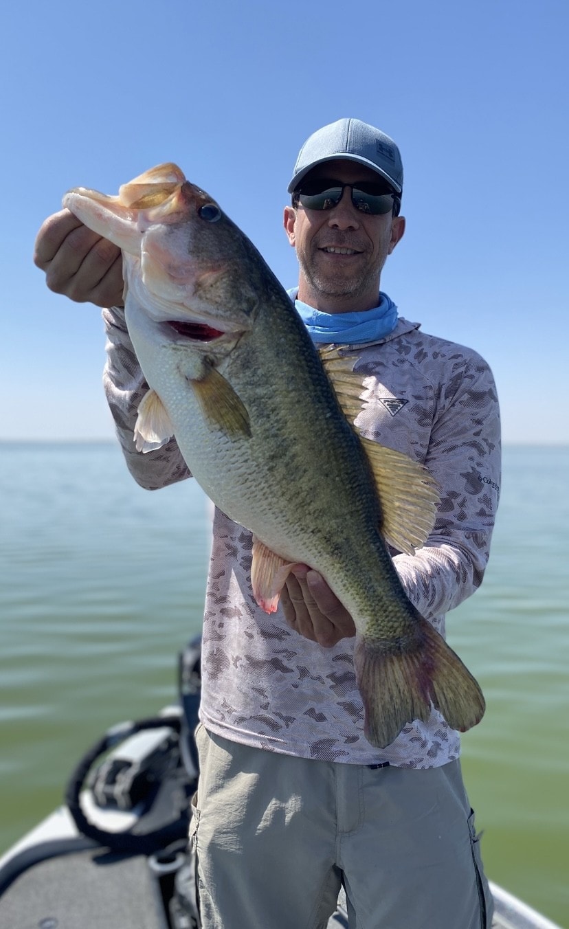 Man in Columbia shirt holding bass on clear blue day
