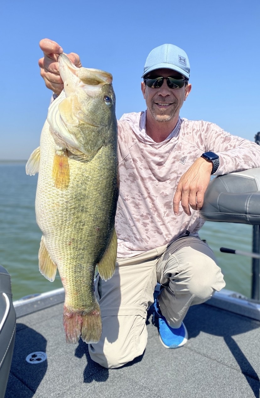 Man in Under Armour cap holding trophy bass on boat