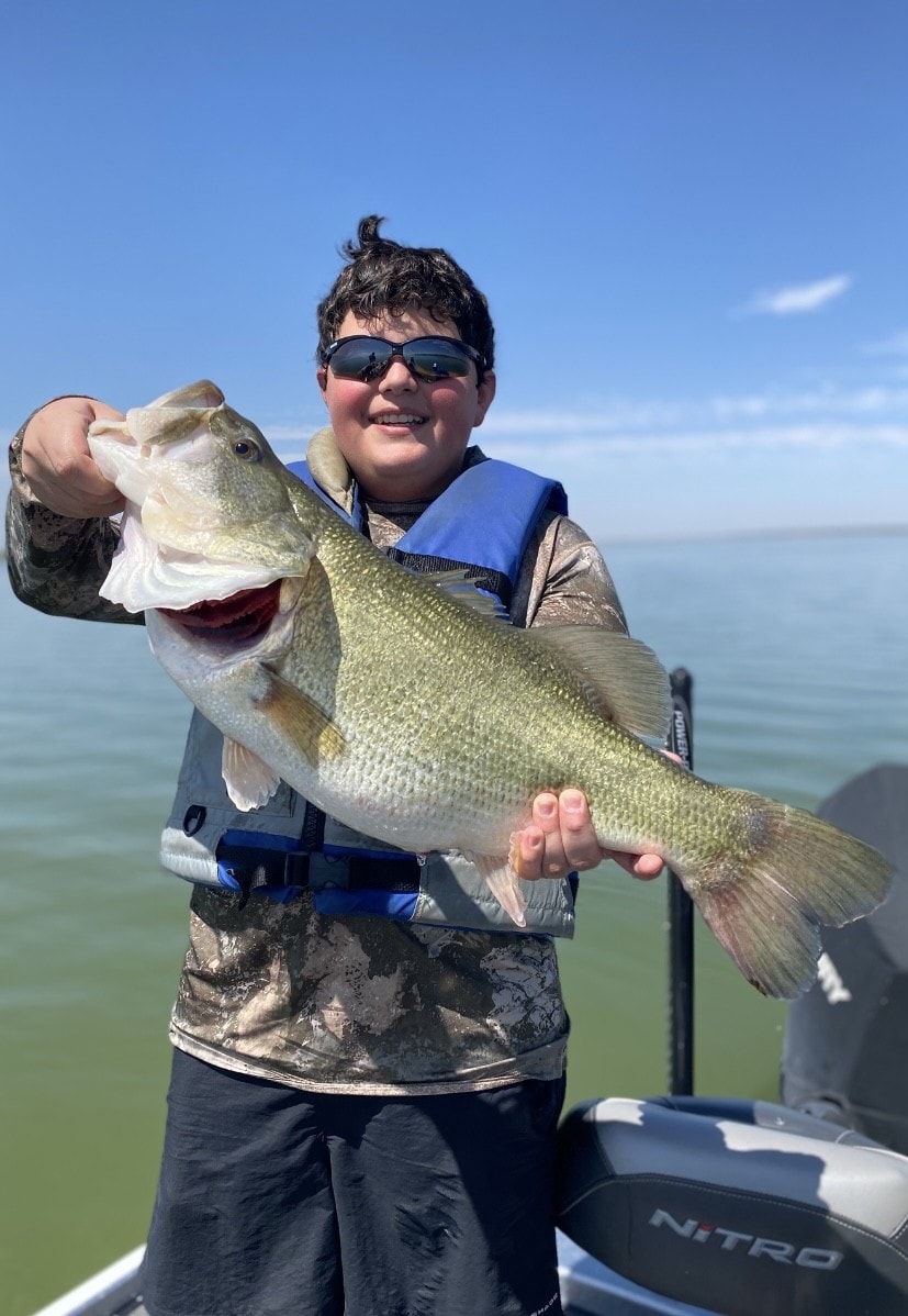 Boy in blue life vest and camo shirt holding giant bass on Nitro boat
