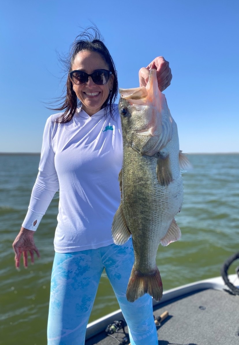 Woman in white shirt and teal leggings holding bass on sunny day