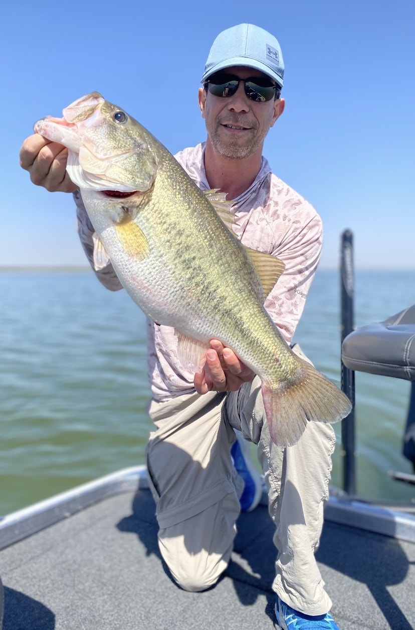 Man in Under Armour cap kneeling with big bass on Nitro boat