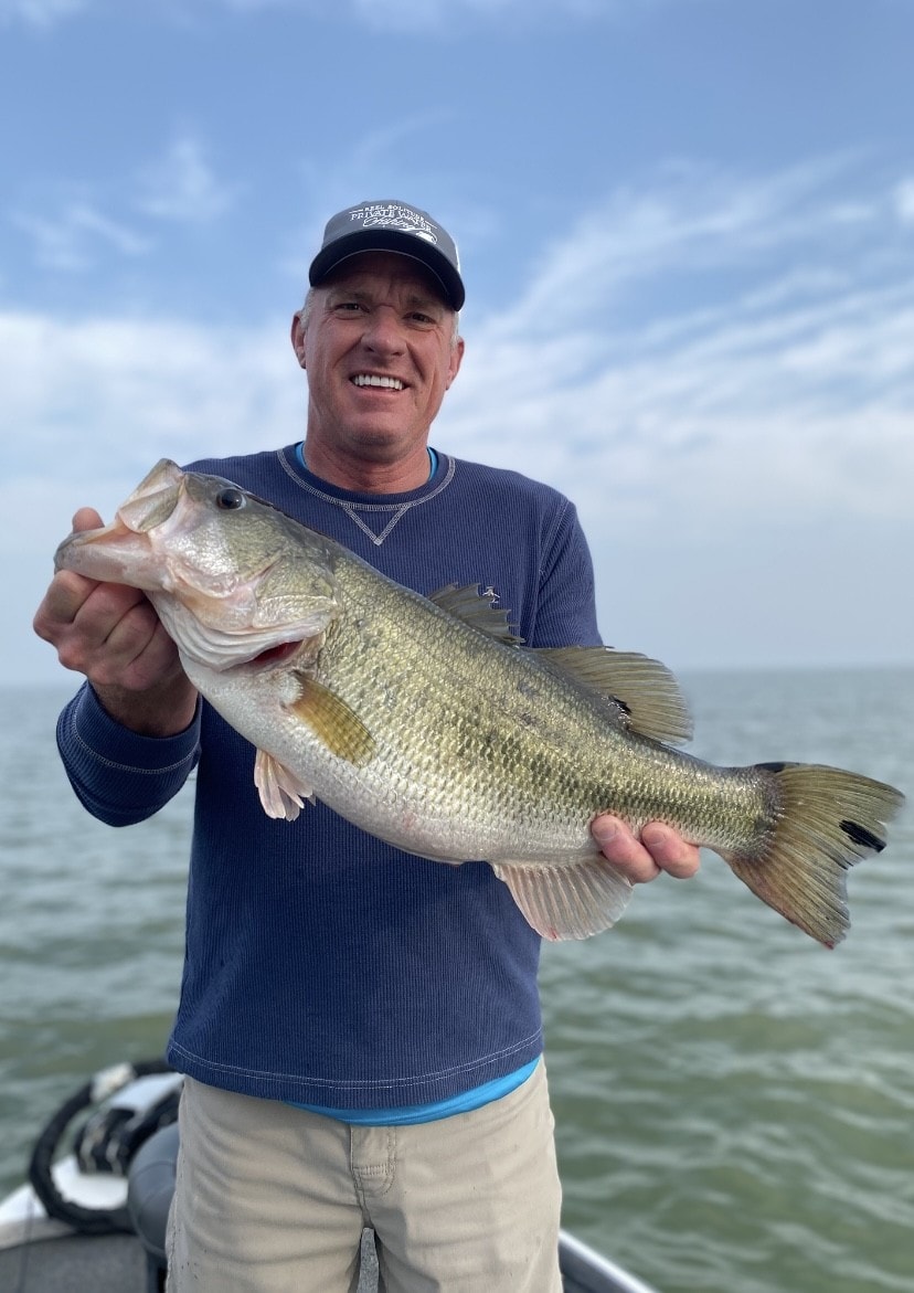 Man in Private Waters cap holding trophy bass on cloudy day