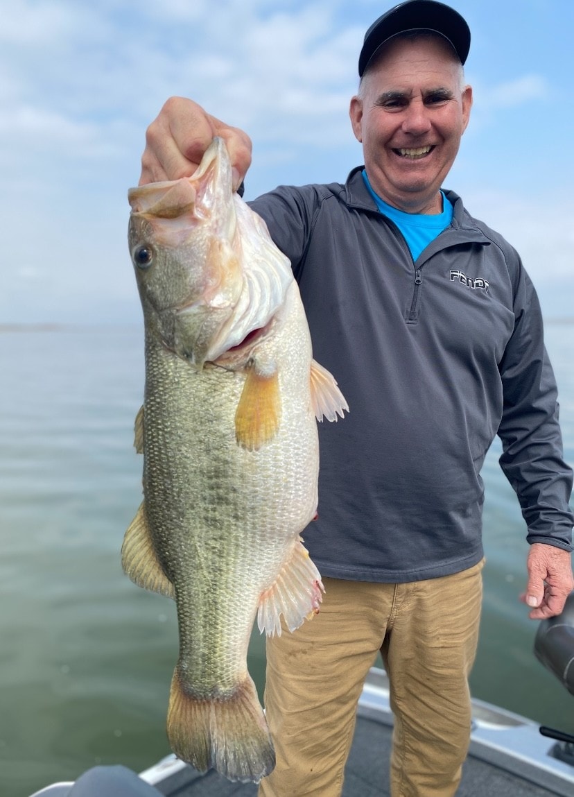 Man in Fenwick jacket holding bass by the lip on cloudy day