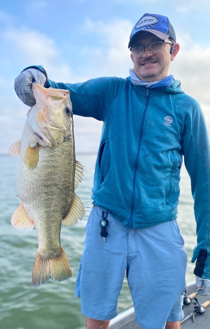 Man in teal Loki hoodie holding bass on cloudy day
