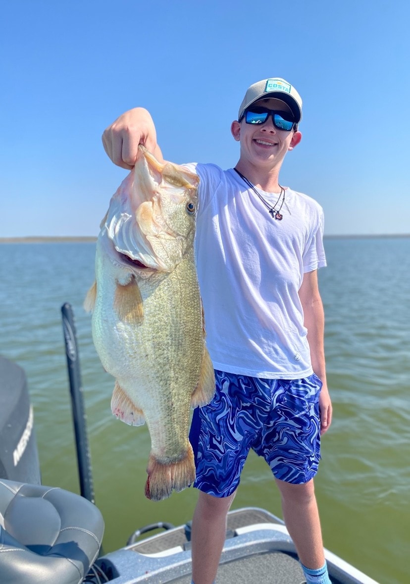Teen in Costa cap and white shirt holding big bass on sunny day