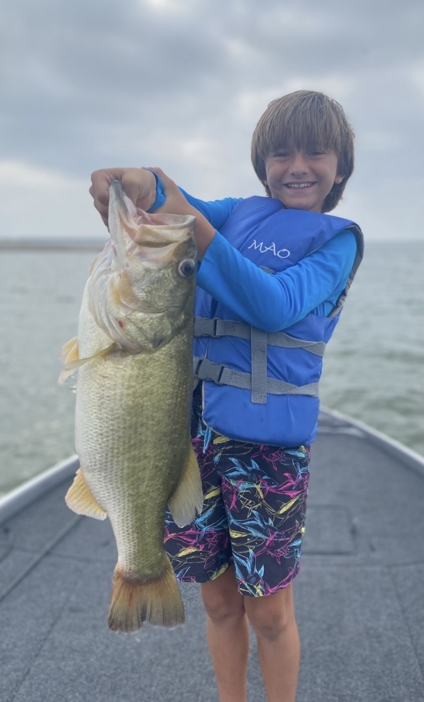 Young boy in blue life vest hugging giant bass on boat