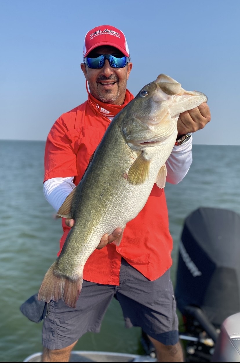 Man in red Pelagic cap holding massive bass on sunny day