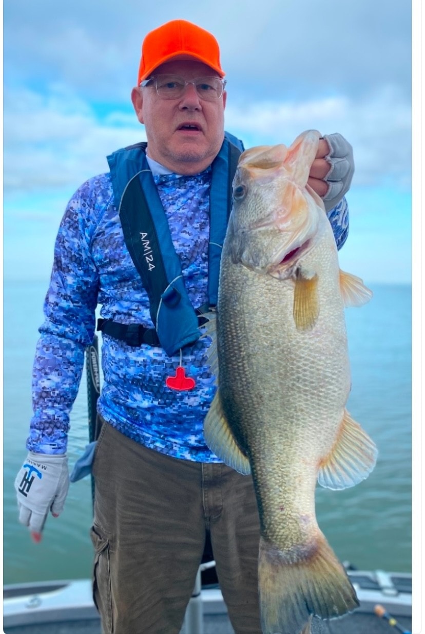 Man in orange cap and blue camo shirt holding big bass on cloudy day