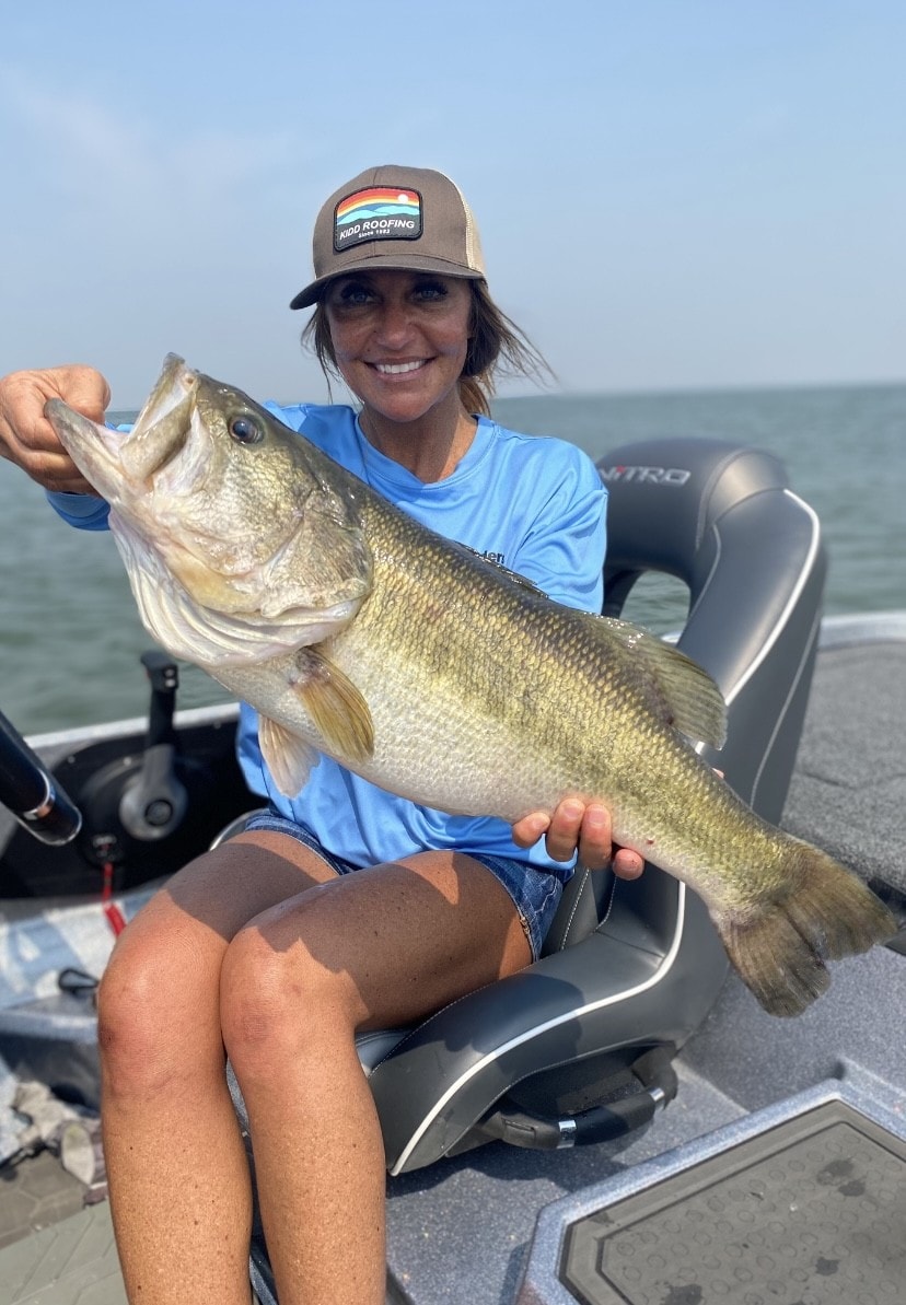 Woman in Kidd Roofing cap holding giant bass on Nitro boat