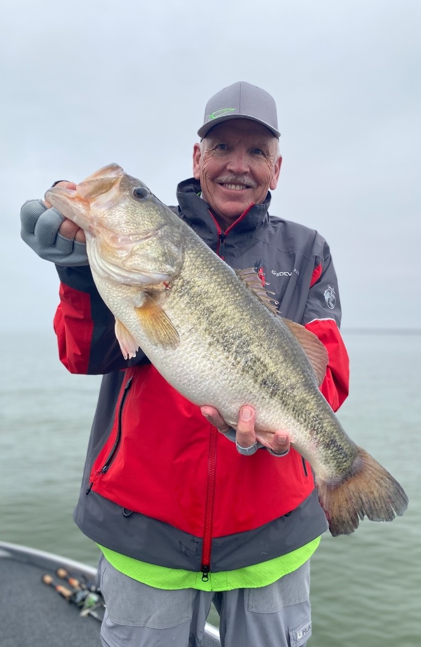 Man in GuideWear jacket holding massive bass on foggy day