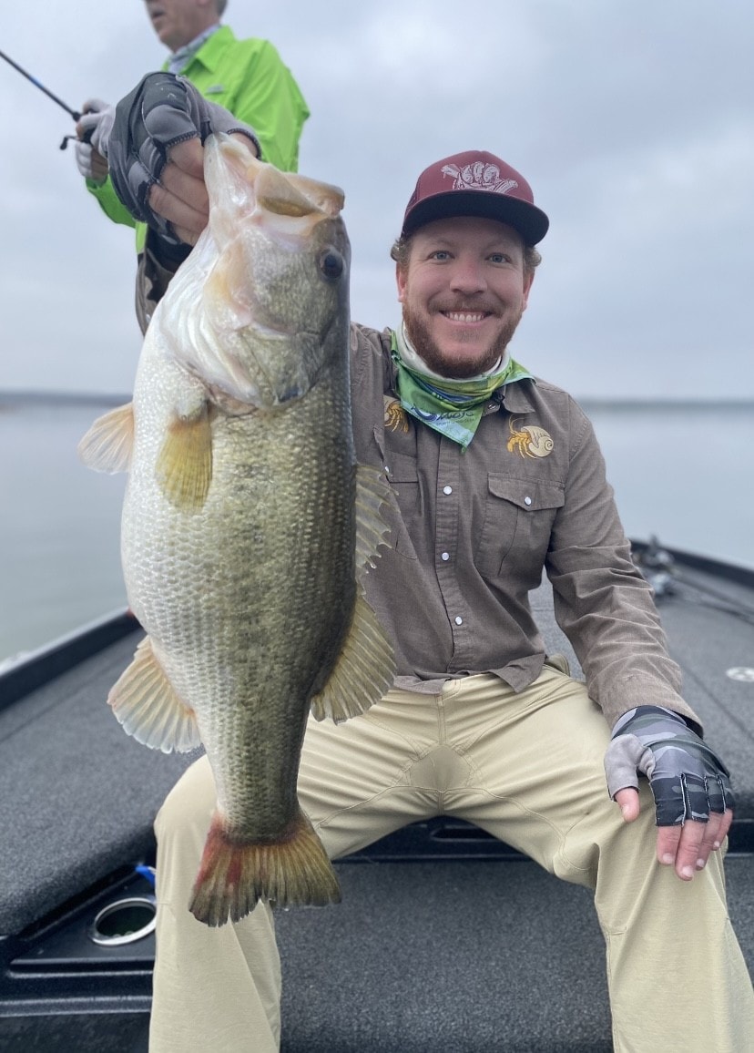 Young man in maroon cap holding big bass on cloudy day