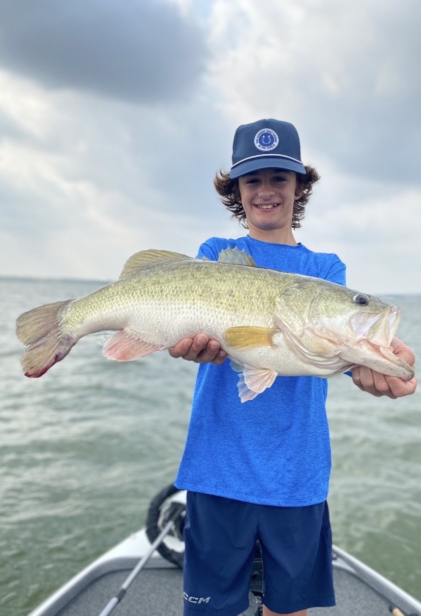 Teen in blue Colts cap holding large bass on overcast day