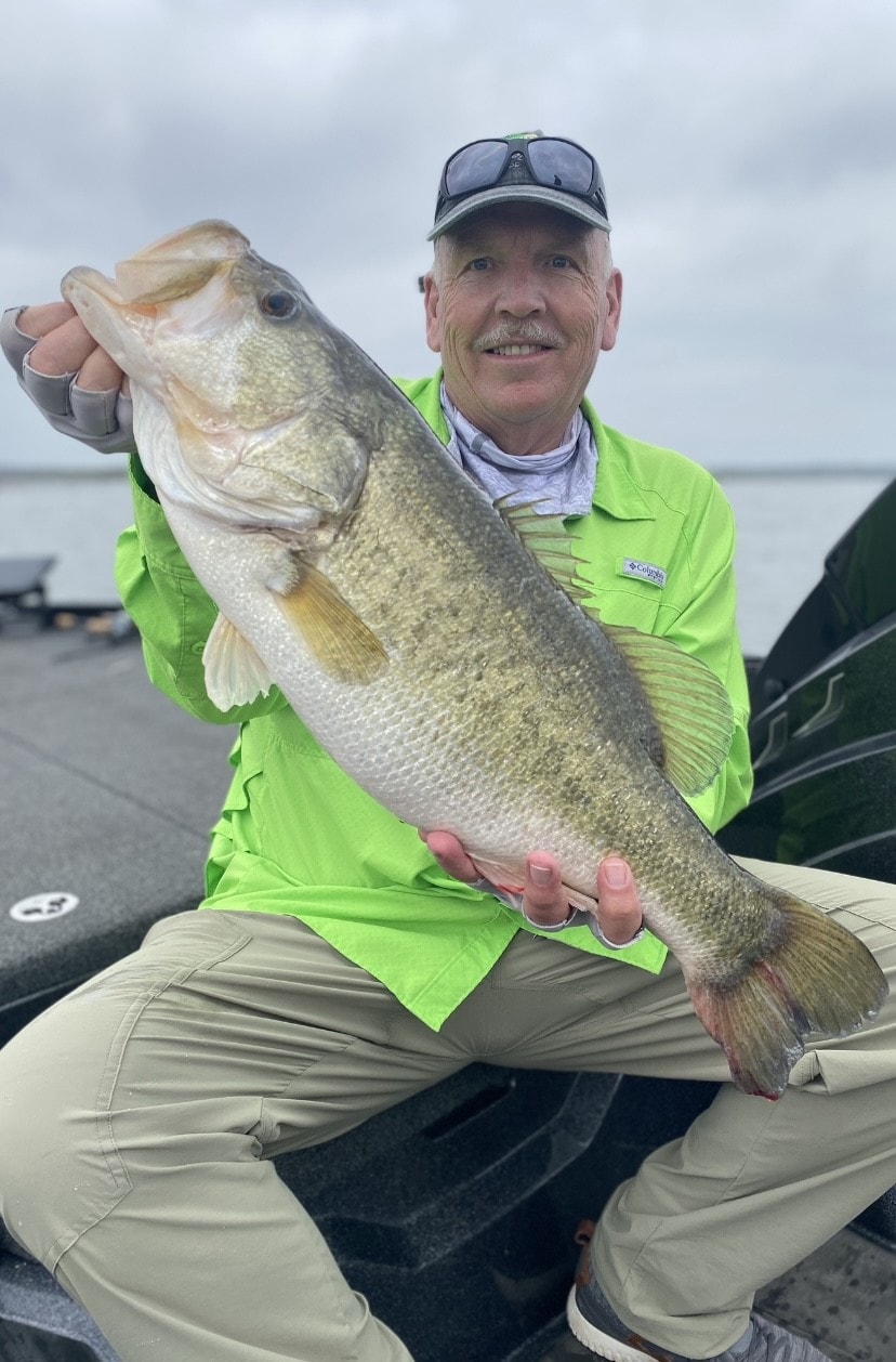 Man in green Columbia shirt holding big bass on cloudy day