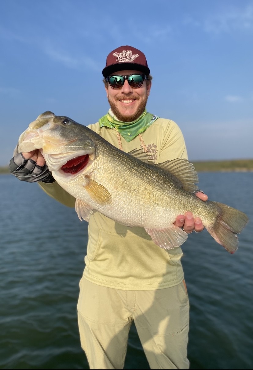 Young man in maroon cap holding giant bass on sunny day