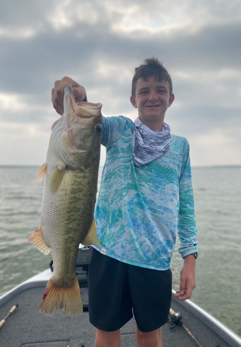 Young boy in teal fishing shirt holding big bass on cloudy day