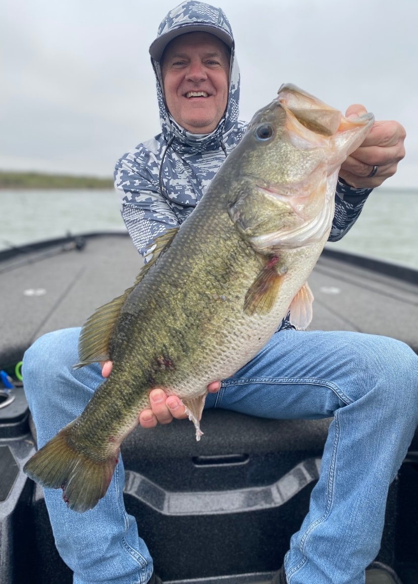 Man in camo gaiter holding giant bass on cloudy day