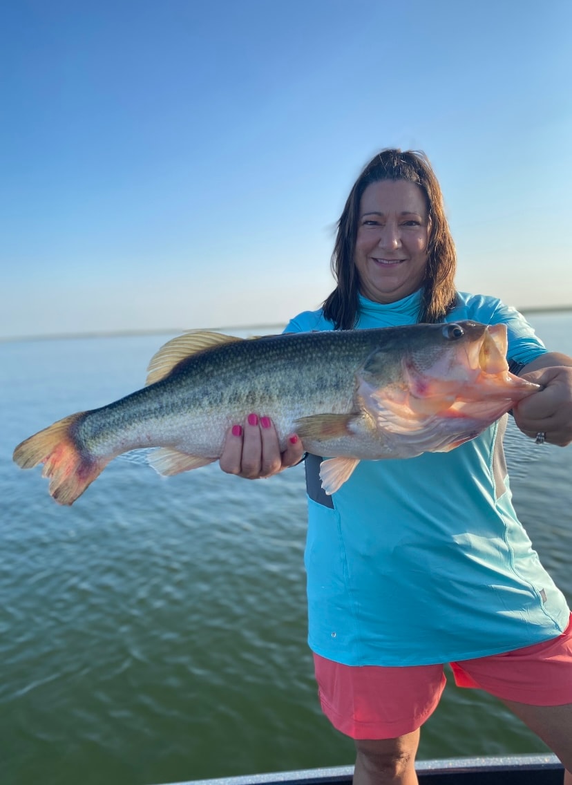 Woman in teal shirt holding big bass on calm sunny day
