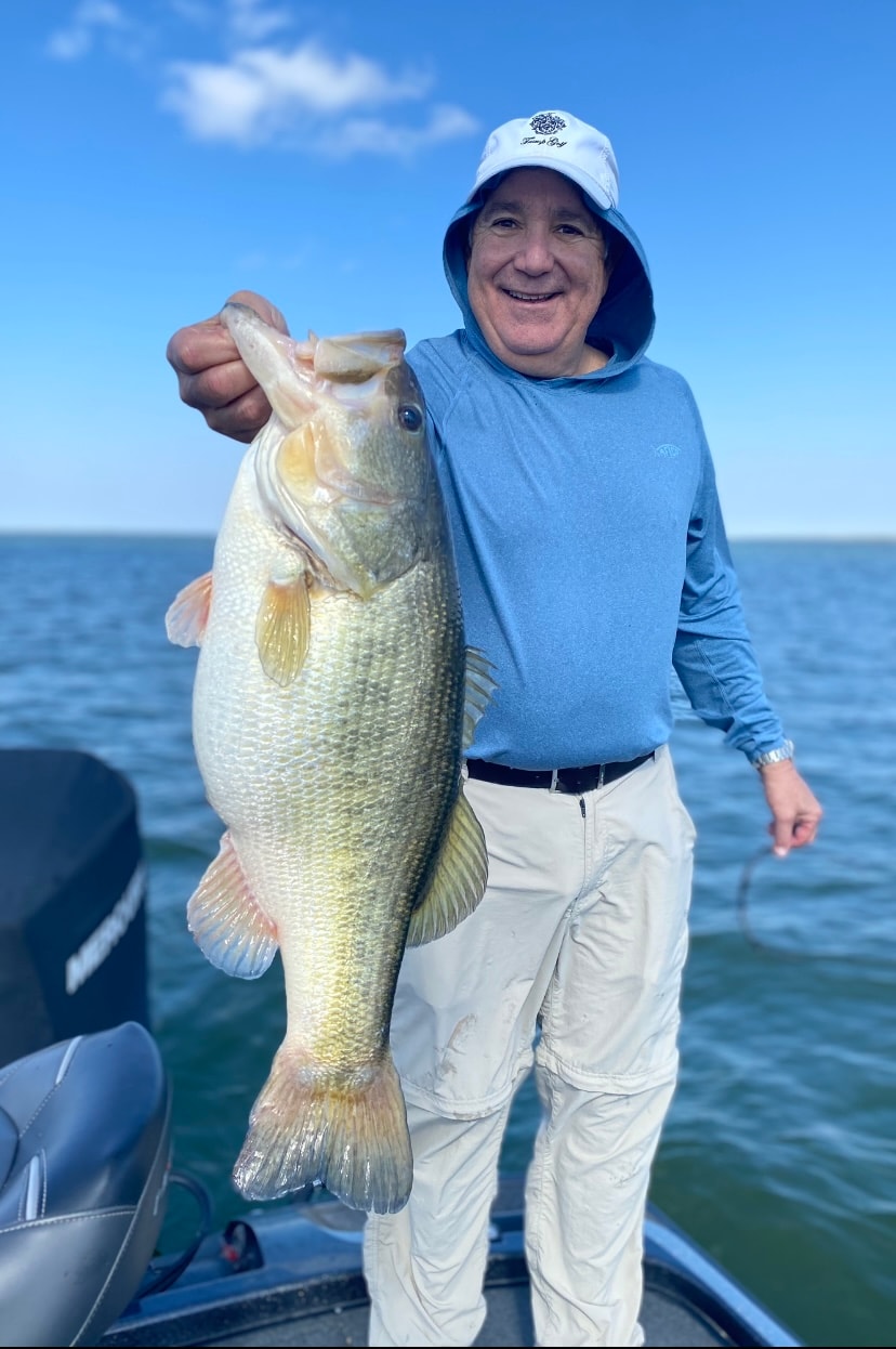 Man in Trump Golf cap holding golden bass on sunny day