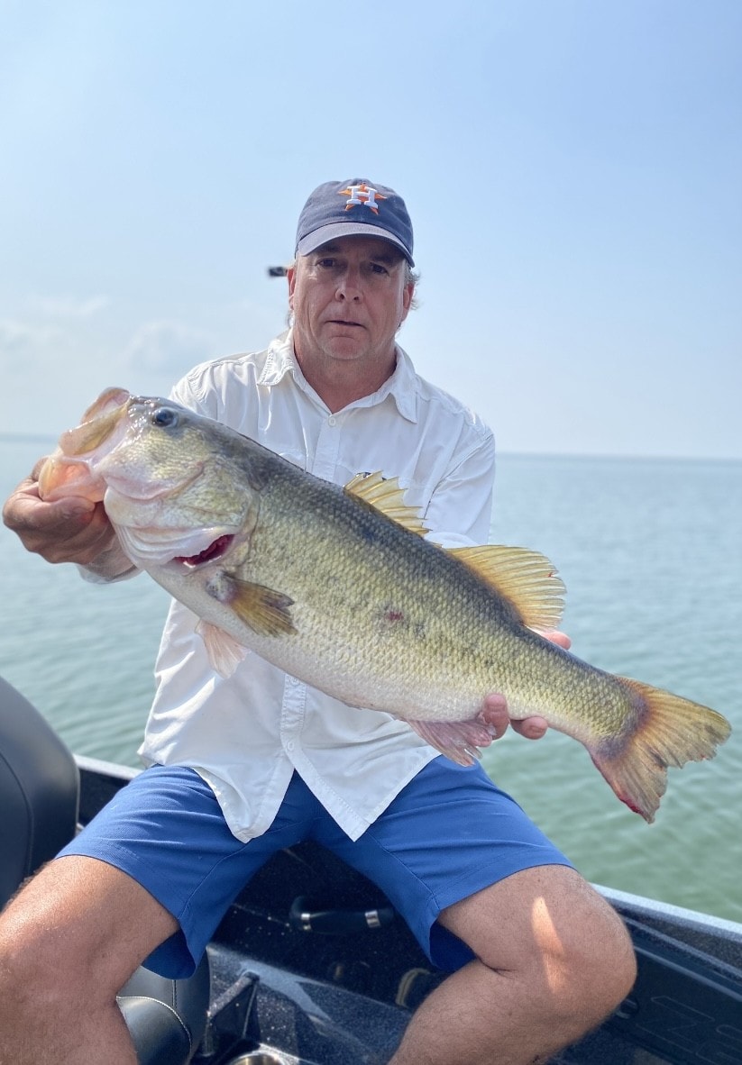 Man in Astros cap holding big bass on sunny day on Lake Falcon