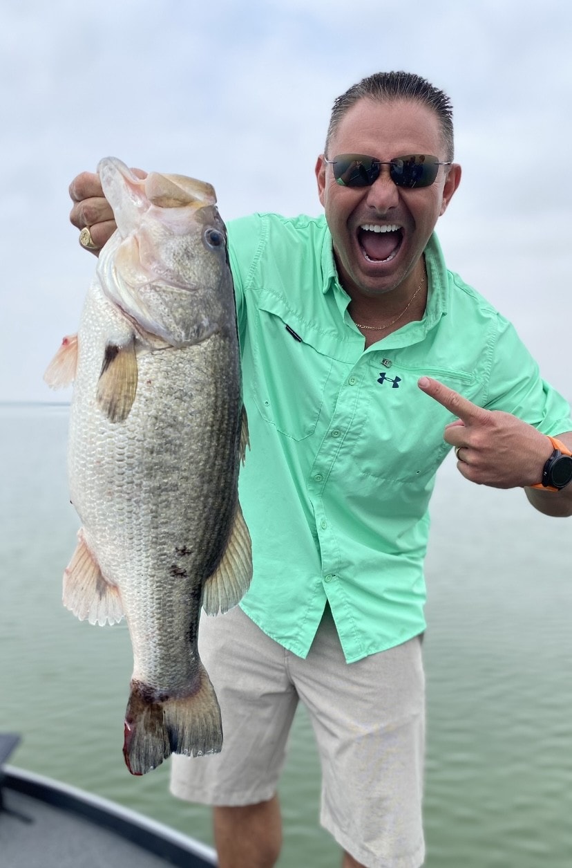 Man in green Under Armour shirt pointing at big bass on cloudy day