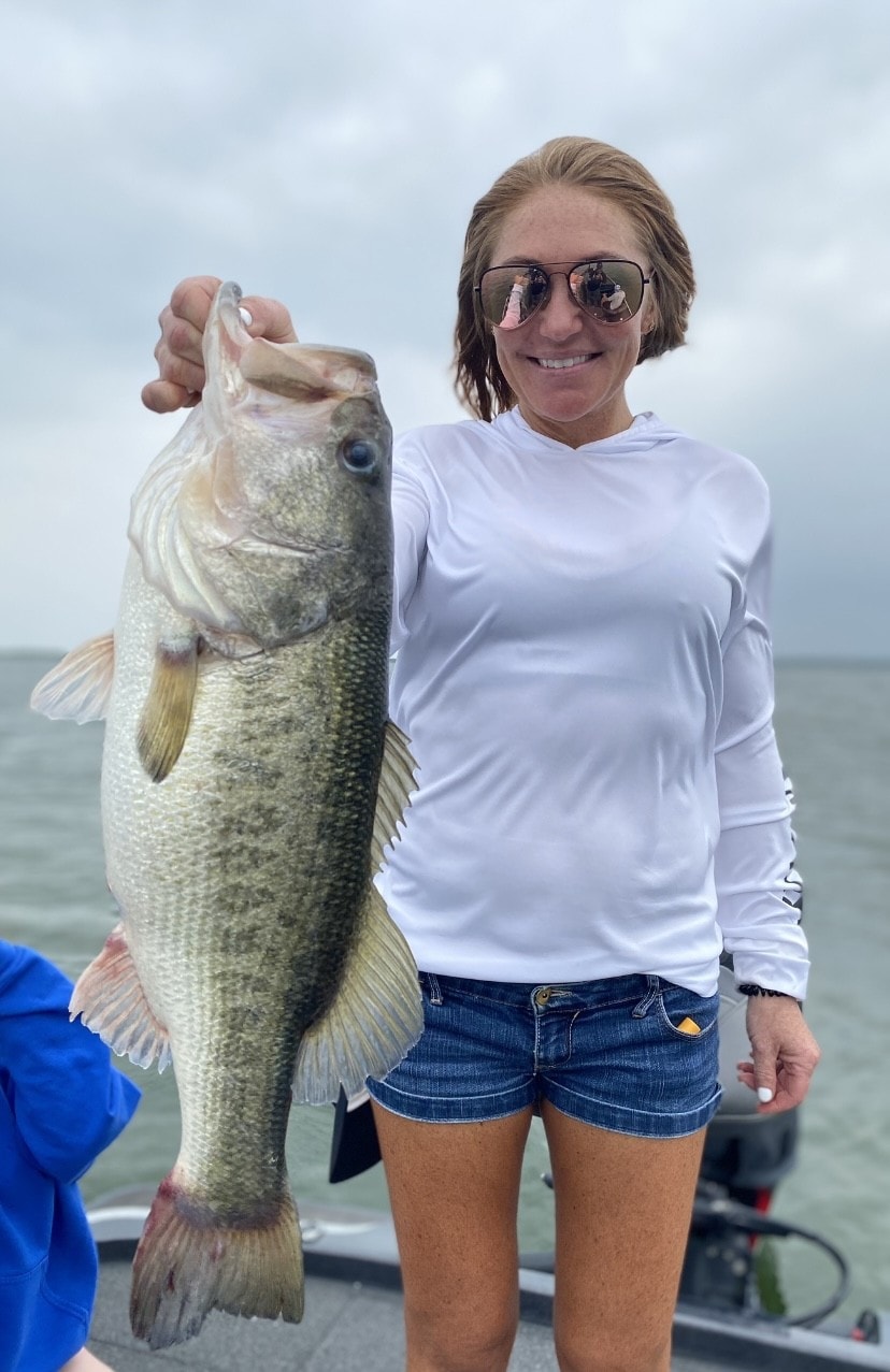 Woman in white hoodie holding trophy bass on cloudy day