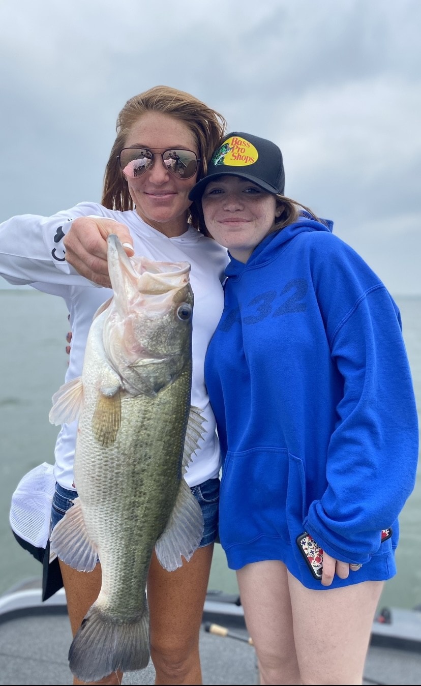Woman and teen in Bass Pro cap holding bass on cloudy day