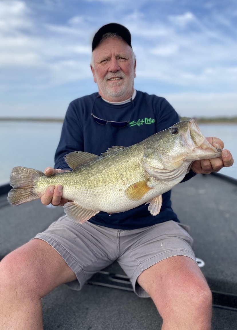 Older man in Salt Life shirt holding big bass on partly cloudy day